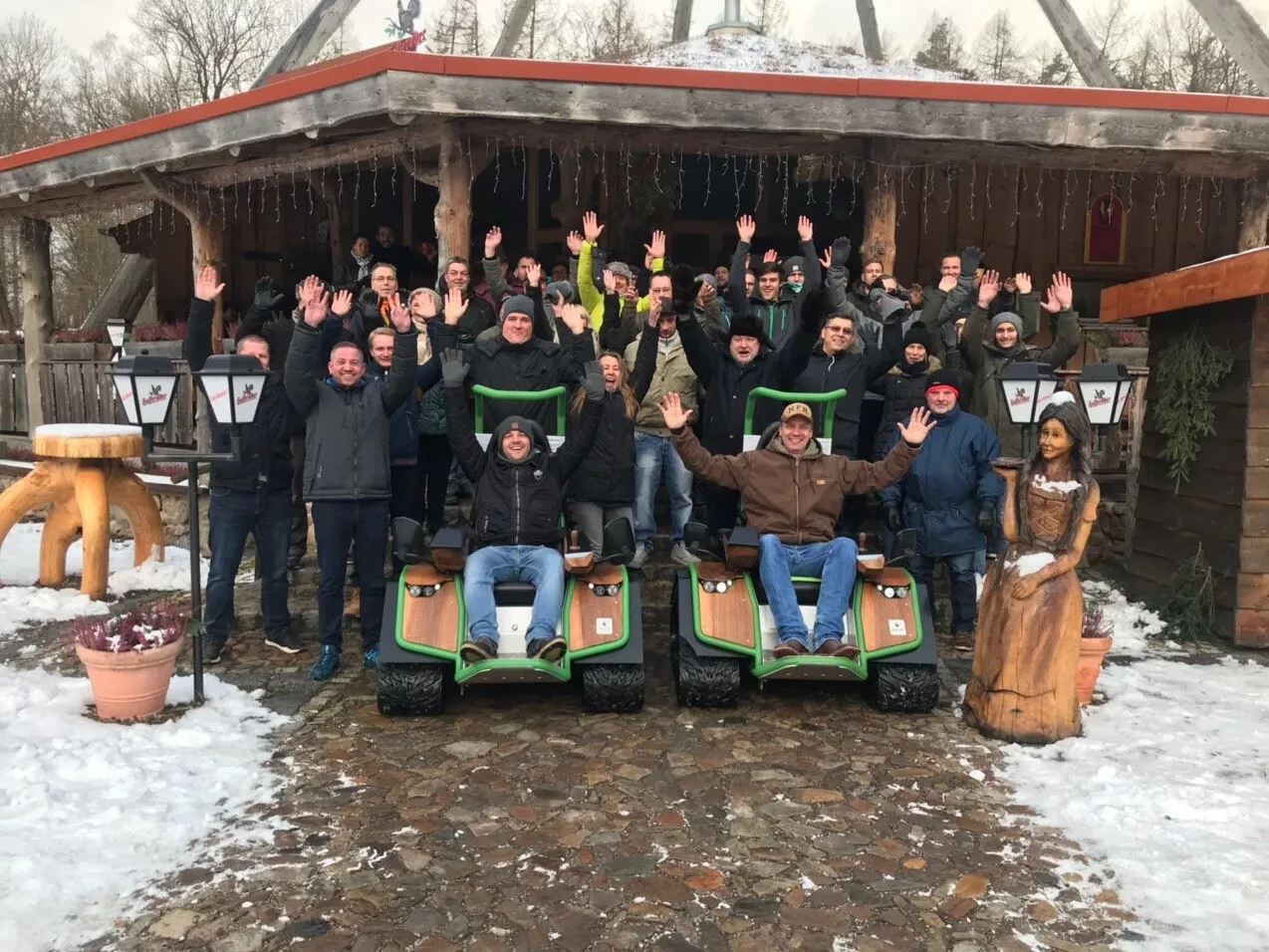 Gruppe von Menschen winkt vor rustikalem Gebäude.